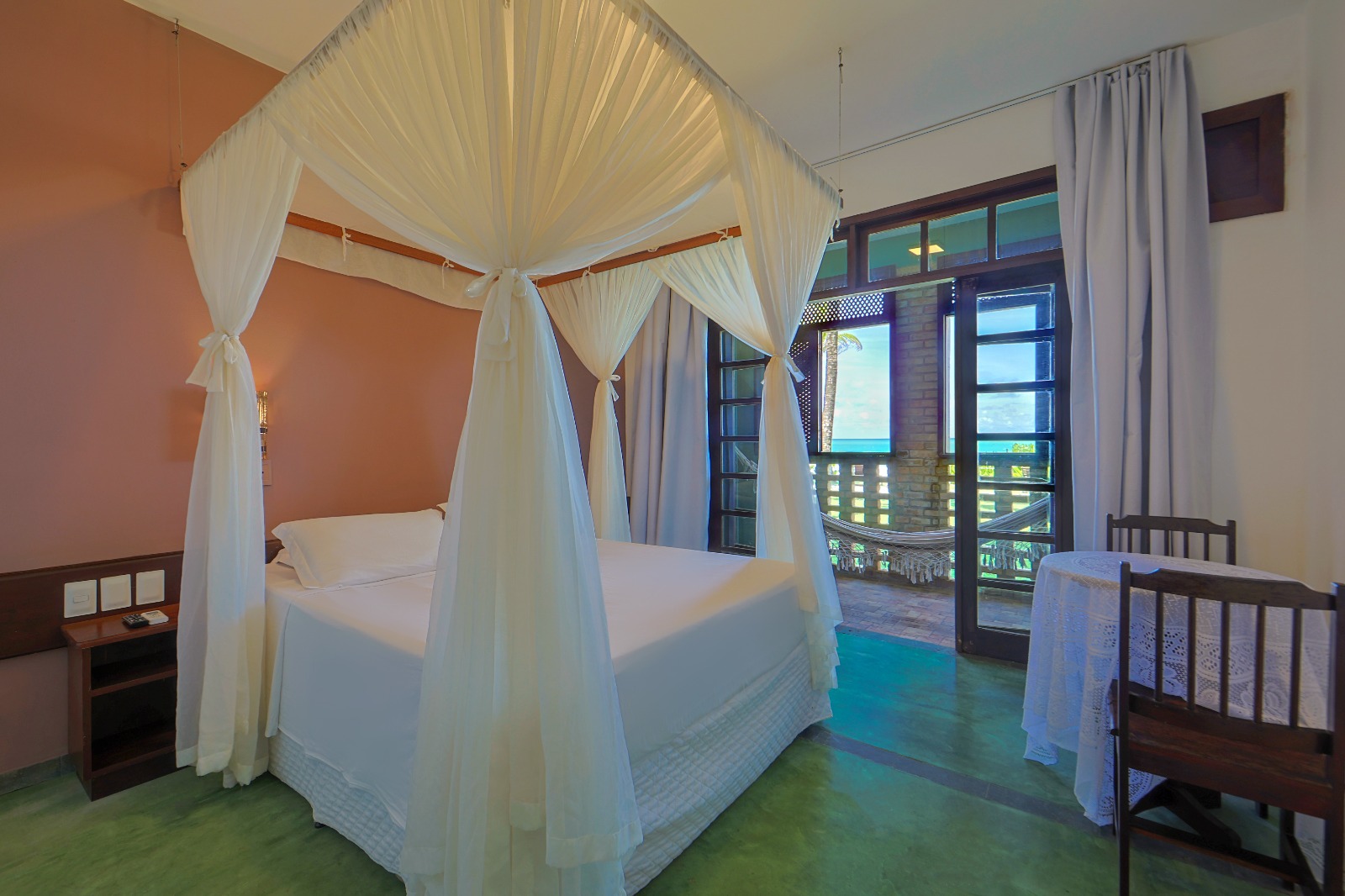 Quarto amplo com cama de dossel e varanda com rede e vista para o mar